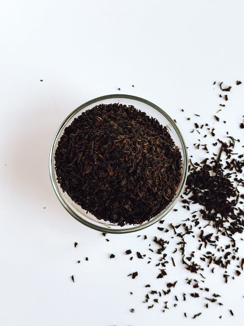 Glass bowl filled with Everlastea organic English breakfast black tea leaves on a white background